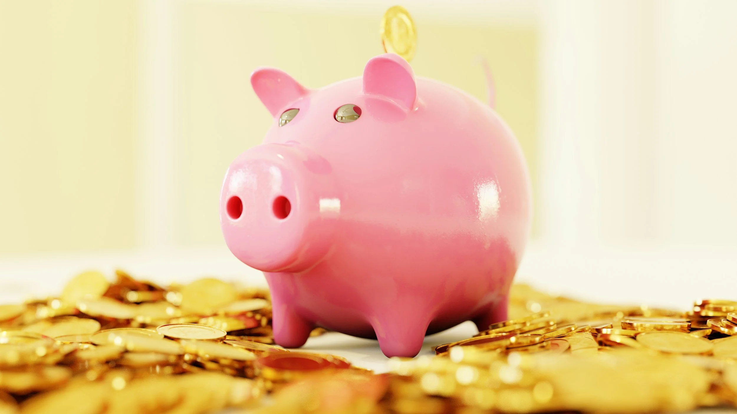 Pink piggy bank surrounded by gold coins on a white surface.