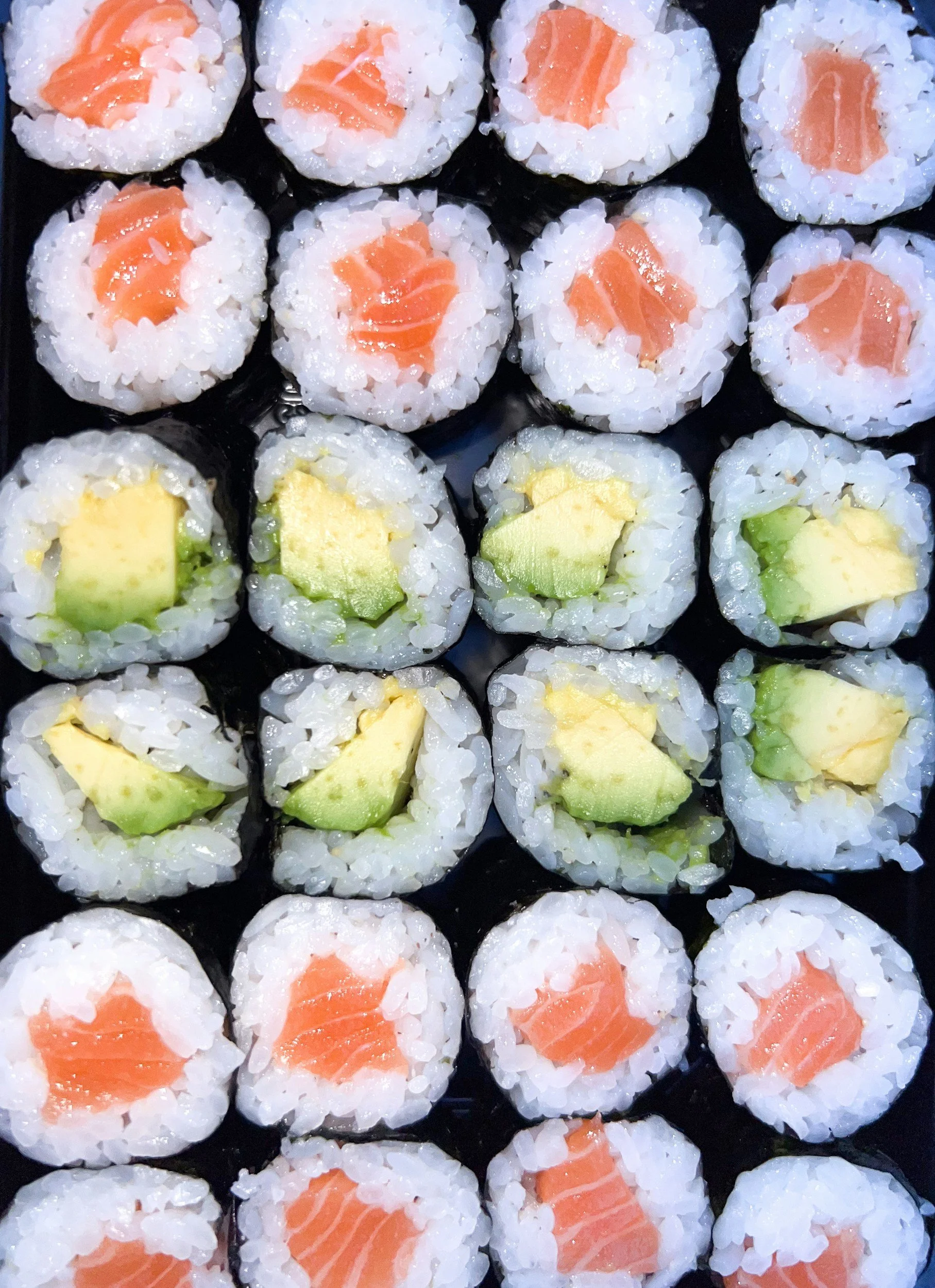 Close-up view of several pieces of sushi rolls with salmon and avocado inside, arranged on a black surface.
