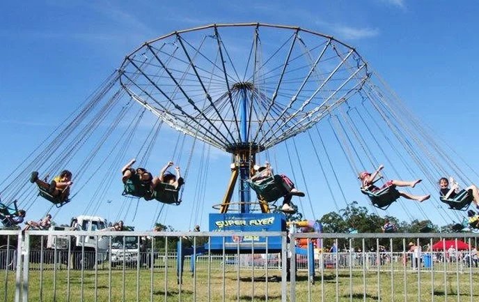 People riding a purple swing ride at an amusement park on a clear day.