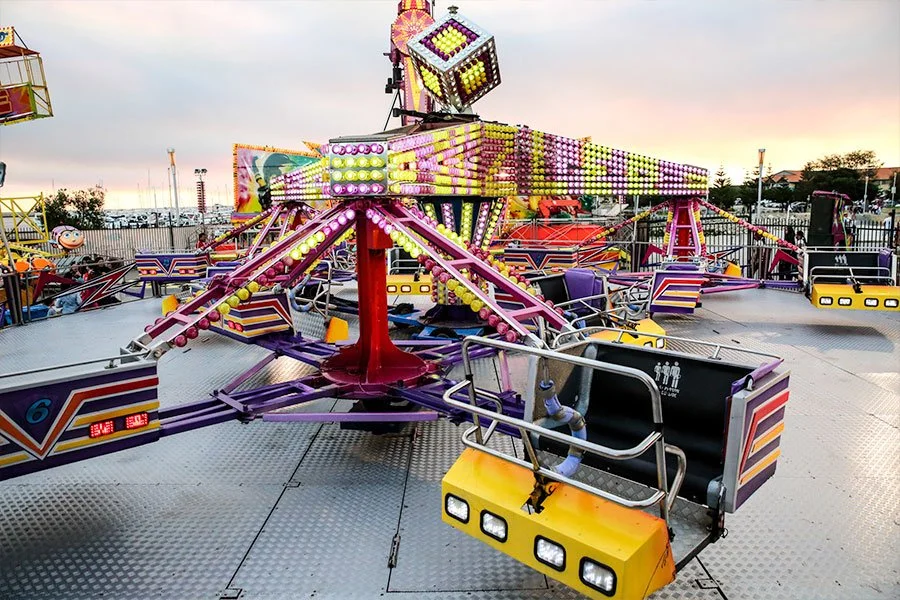 Colorful amusement park ride with suspended seats, illuminated with bright lights, at dusk.