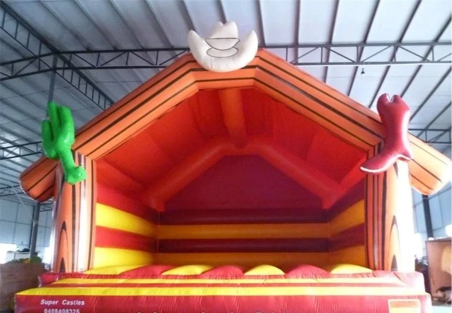 Colorful inflatable house with a peaked roof, decorated with a white star at the top, a green cactus on the left, and a pink cowboy boot on the right.
