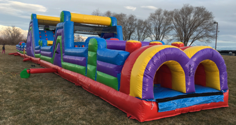 Colorful inflatable obstacle course set up outdoors on grass, with trees and cloudy sky in the background.