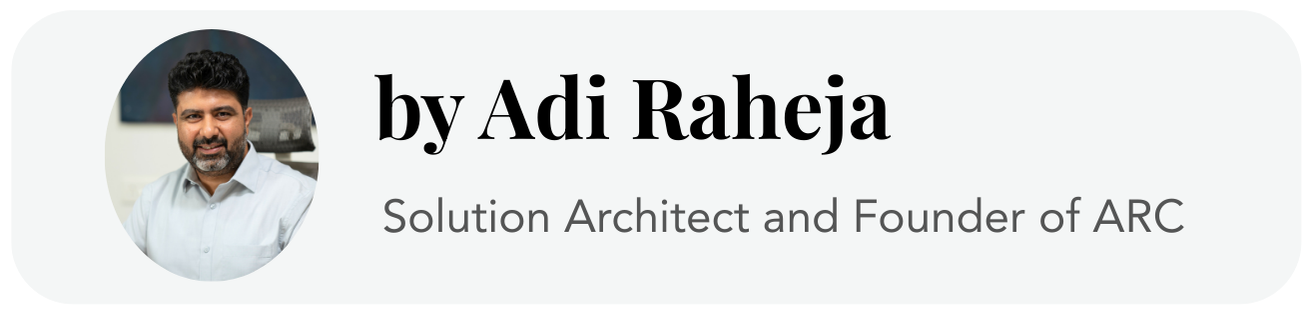 A headshot of a man with dark hair and a beard wearing a white shirt, smiling, with a blurred background.