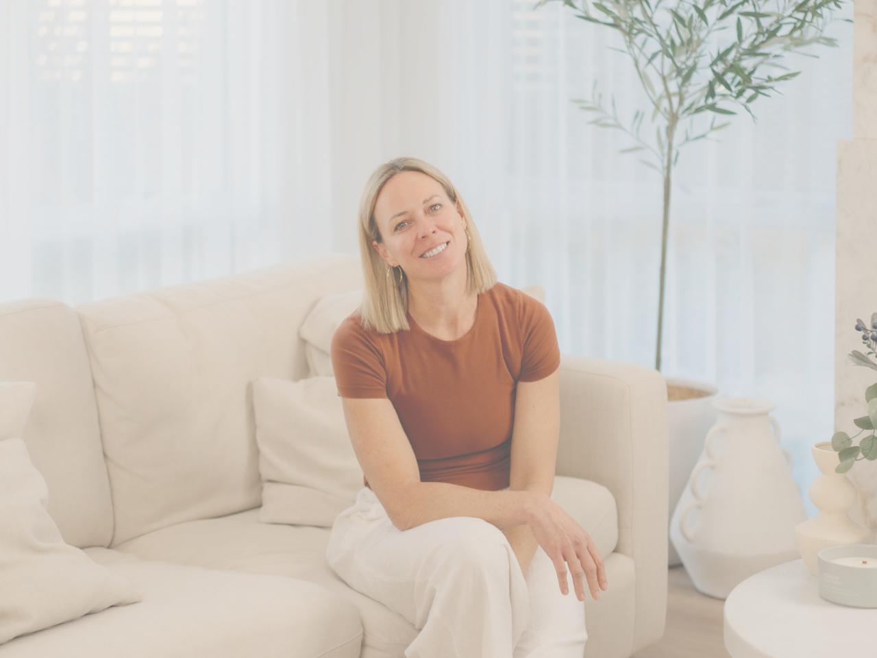 Abbey the Midwife sitting in a bright living room and smiling at the camera.