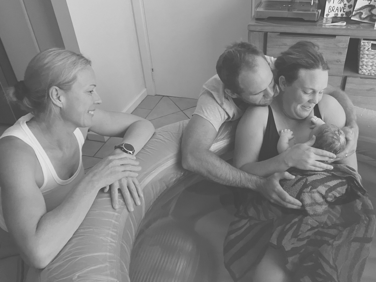 Mother holding her newborn after a homebirth while supported by her partner and midwife.