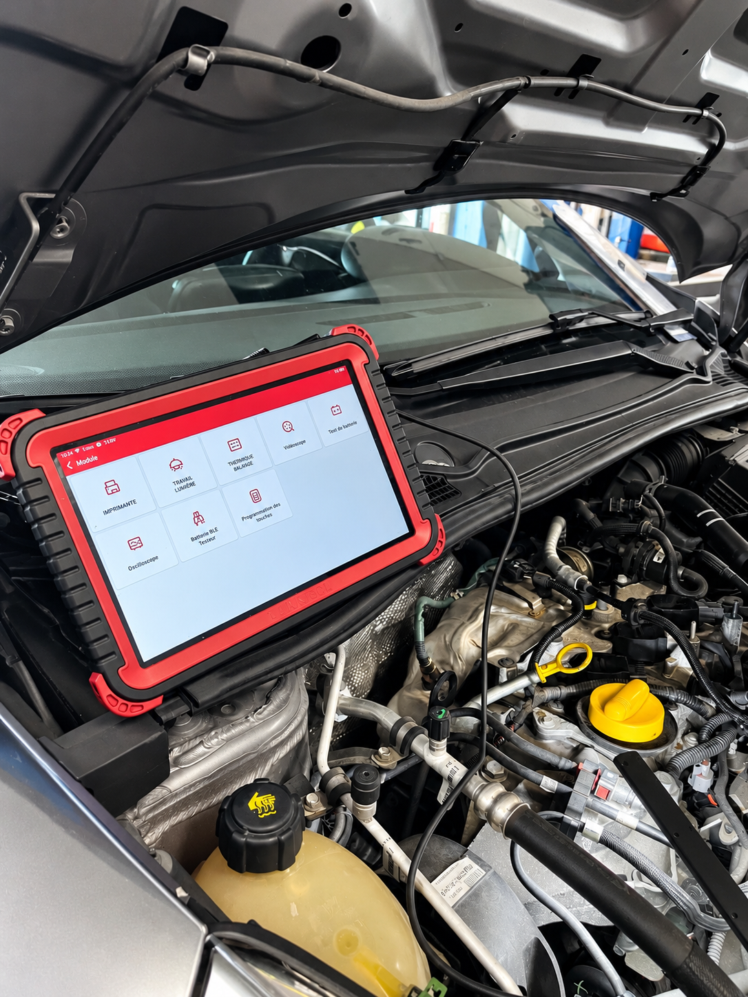 Voiture Volkswagen dans un garage, capot ouvert, vue moteur à gauche. À droite, intérieur de la voiture avec un ordinateur de diagnostic fixé au volant.