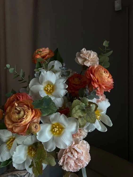 A bouquet of white and orange flowers with green foliage in a dimly lit room.