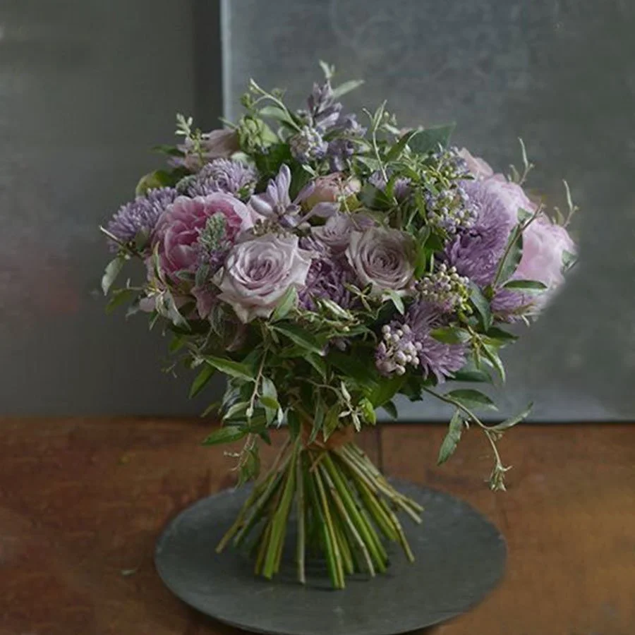 A bouquet of purple and pink flowers with green foliage on a dark round plate.