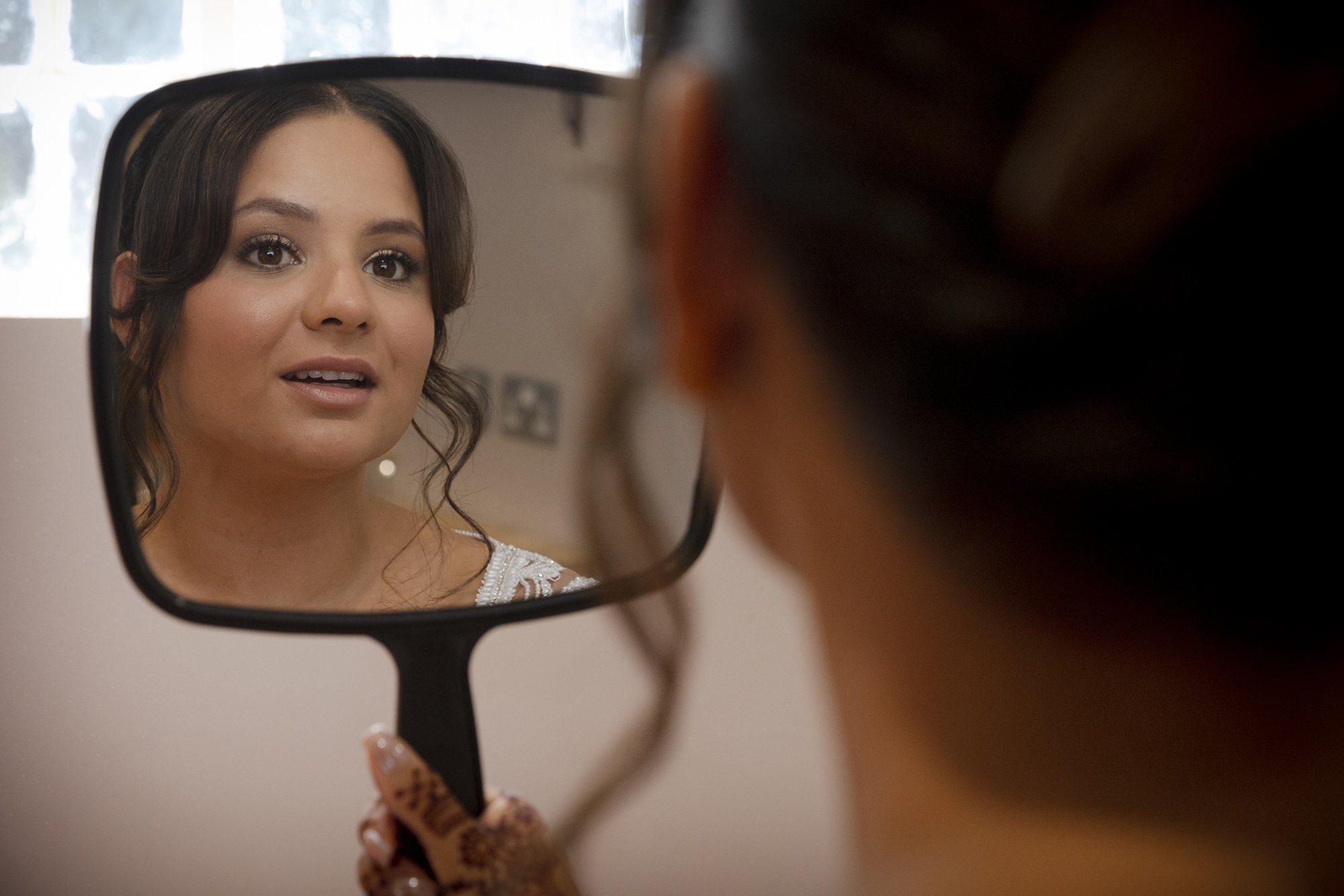 A woman looking in a hand mirror, with her reflection showing her face and expression.