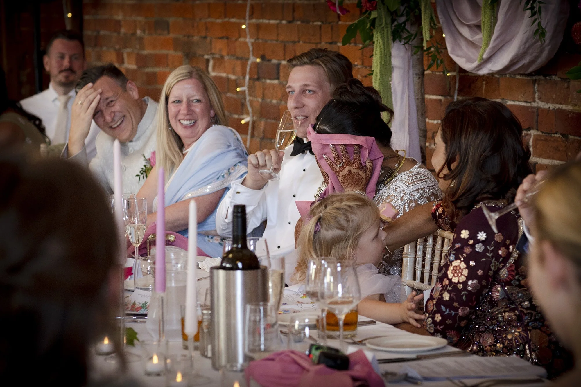 People sitting at a decorated table during a celebration, smiling and laughing, with a brick wall in the background.