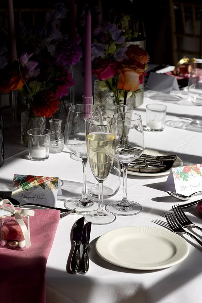 Elegant table setting with champagne glasses, floral centerpieces, candles, and place cards on a white tablecloth.
