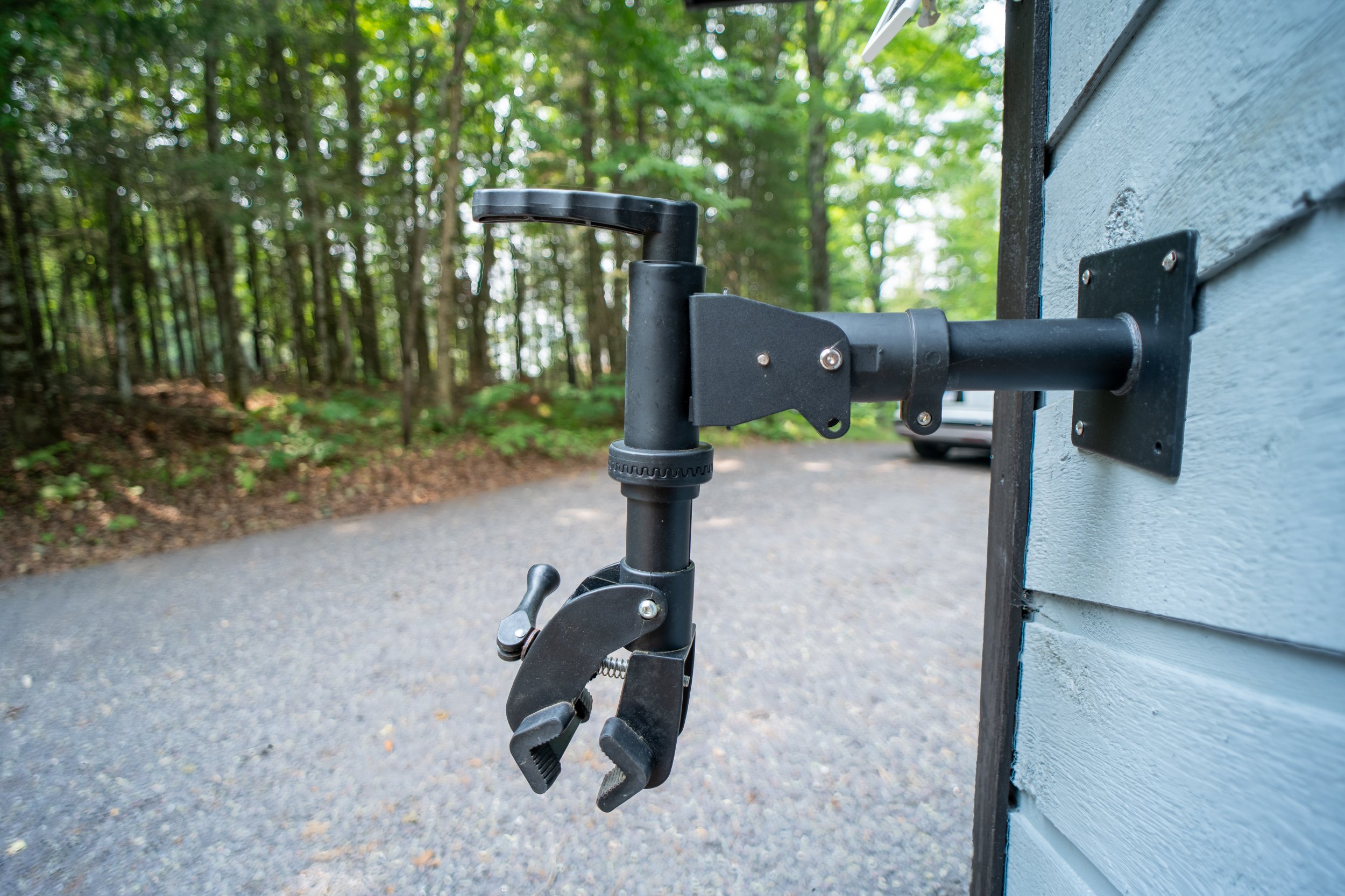 Close-up of a black outdoor faucet with a hose connector, mounted on the side of a blue and gray wooden shed, in a wooded backyard.