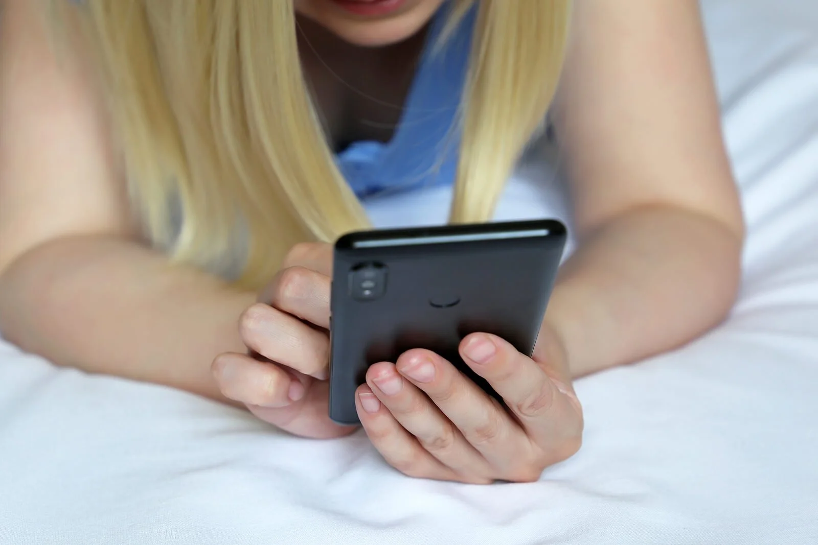 A close up of a teen typing on their phone while laying in bed. Learn how social media can influcene our eating habits through eating disorder treatment in Horsham, PA. Contact an eating disorder therapist in Horsham, PA to learn more about body dysm