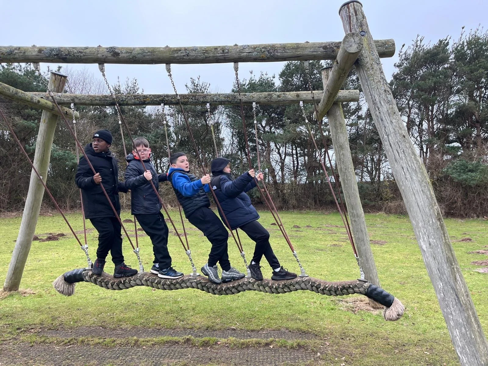 four kids on a swing in an outdoor play area