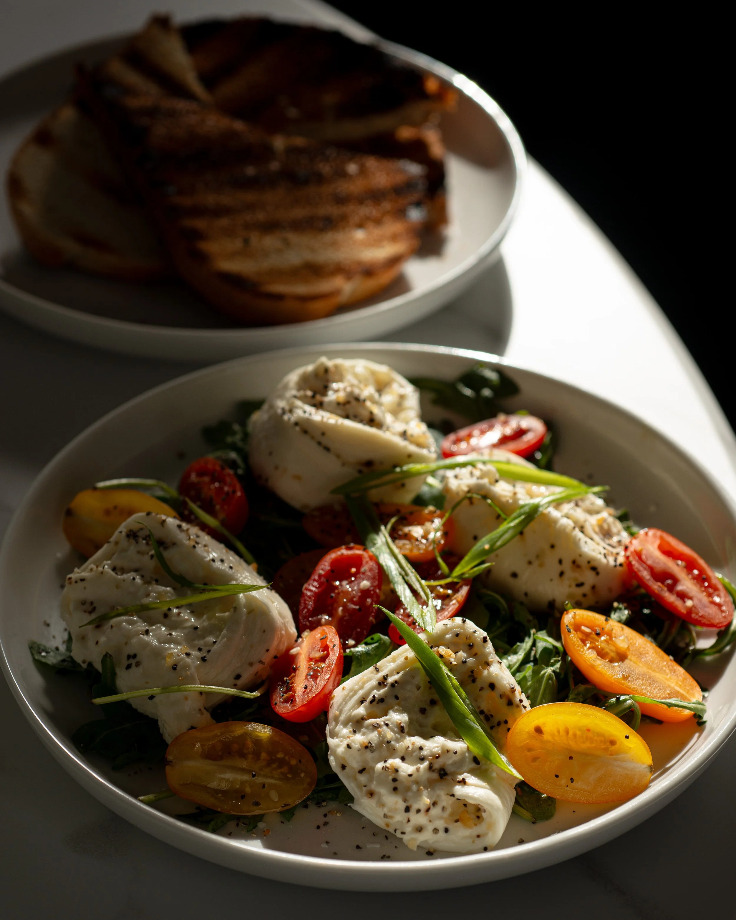Caprese salad with cherry tomatoes, mozzarella, basil, and black pepper, with a side of toasted bread on a white plate.