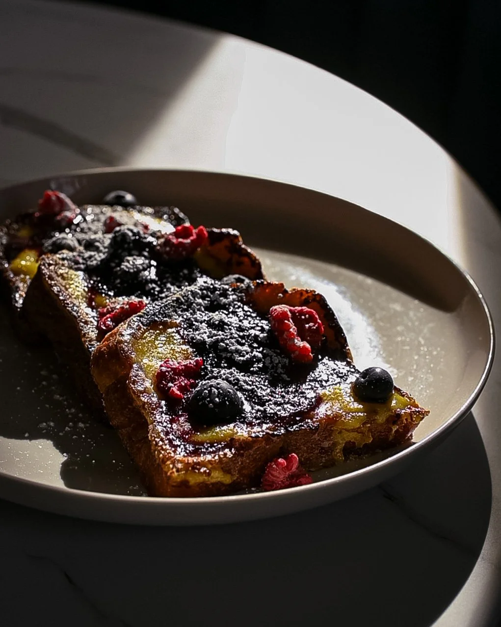 Berry French toast on a white plate with powdered sugar, served with a dark background.