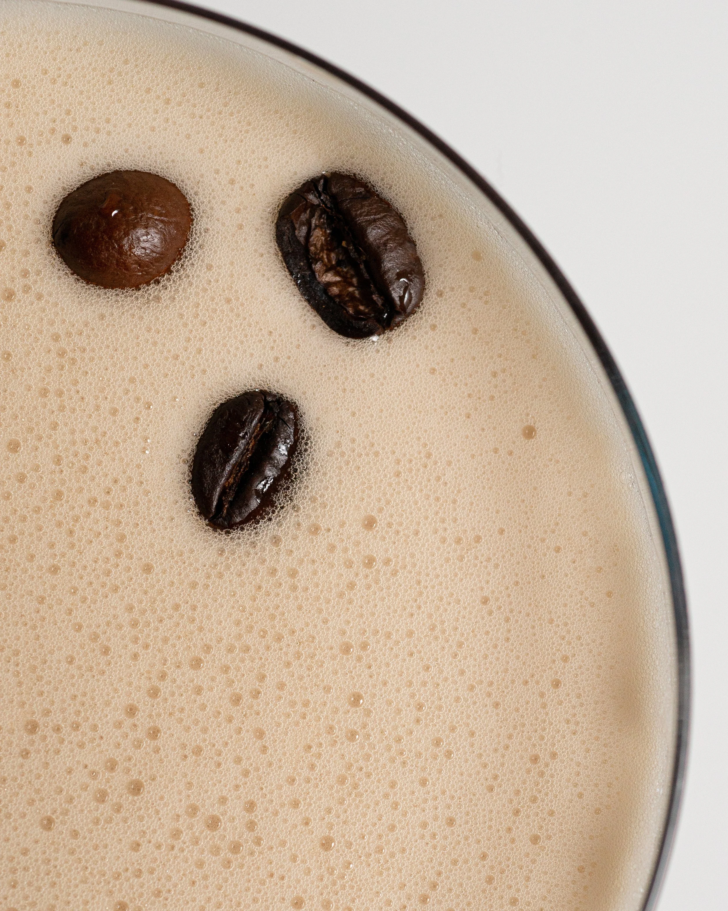 Close-up of a creamy coffee or latte topped with coffee beans floating on the surface.
