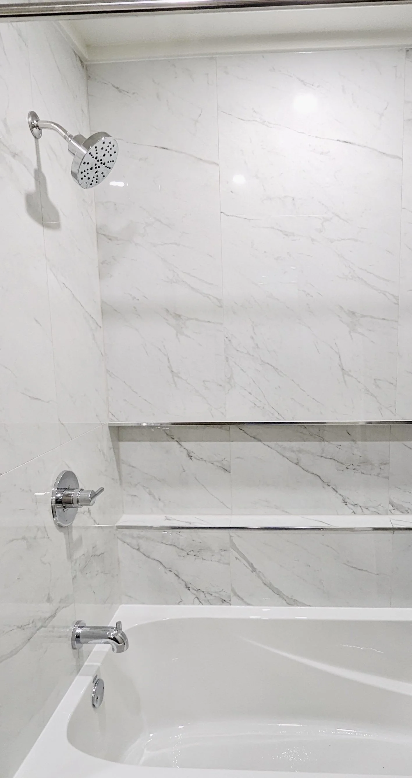 Shower and bathtub combination in a marble-tiled bathroom with a chrome showerhead and controls.