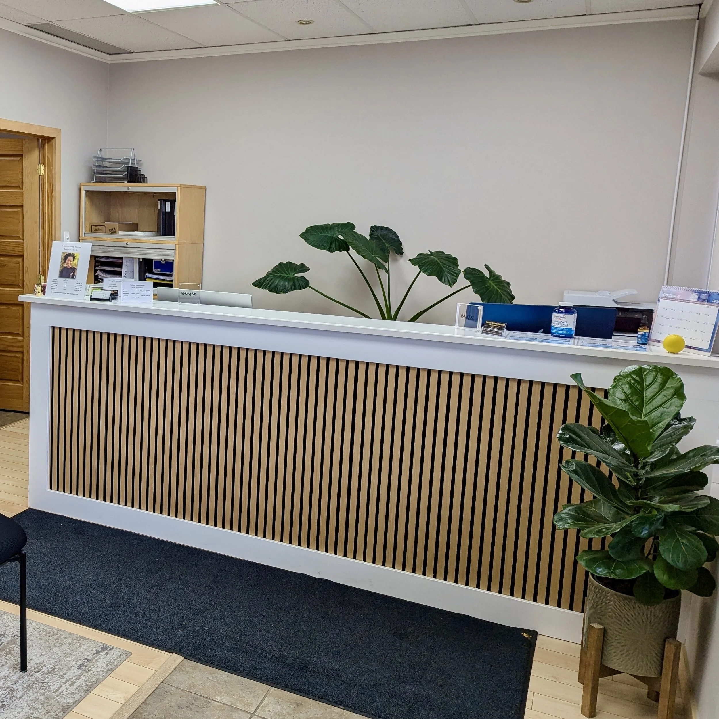 Reception desk with a black and white striped front, potted plants, and office supplies on top, in an office setting.