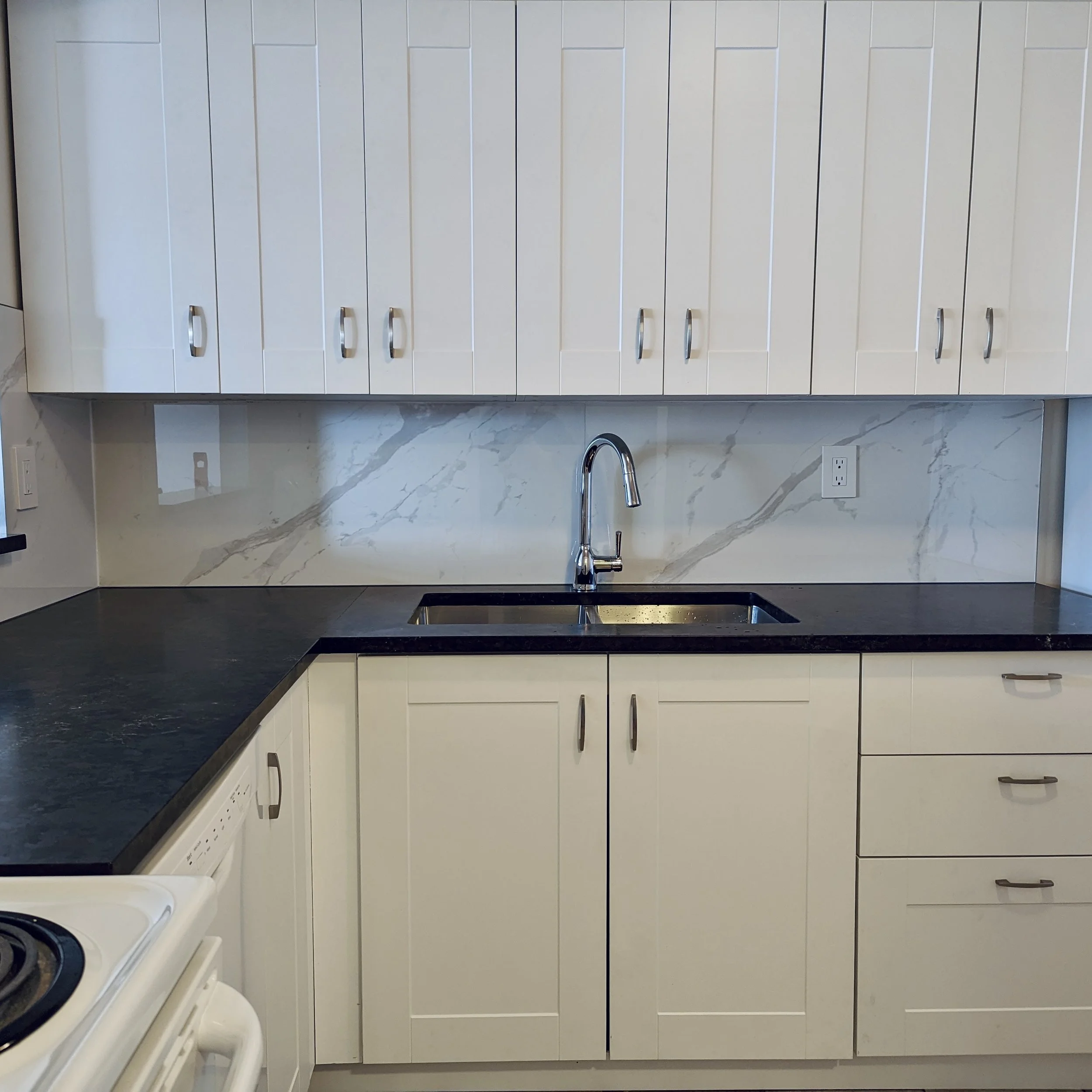 Kitchen with white cabinets, black countertop, and a stainless steel sink with a chrome faucet.