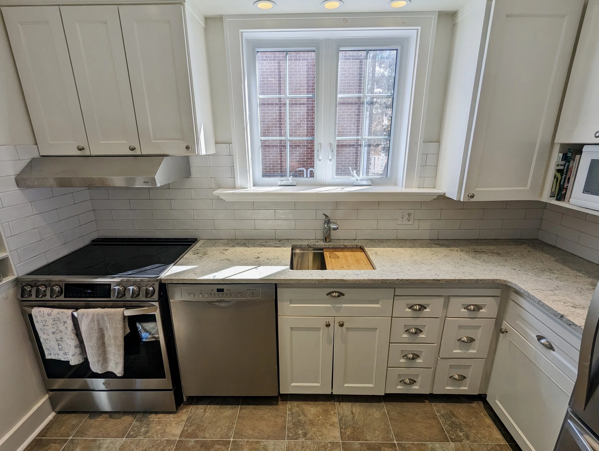 Kitchen with white cabinets, a window above the sink, black stove, dishwasher, microwave, and granite countertops.