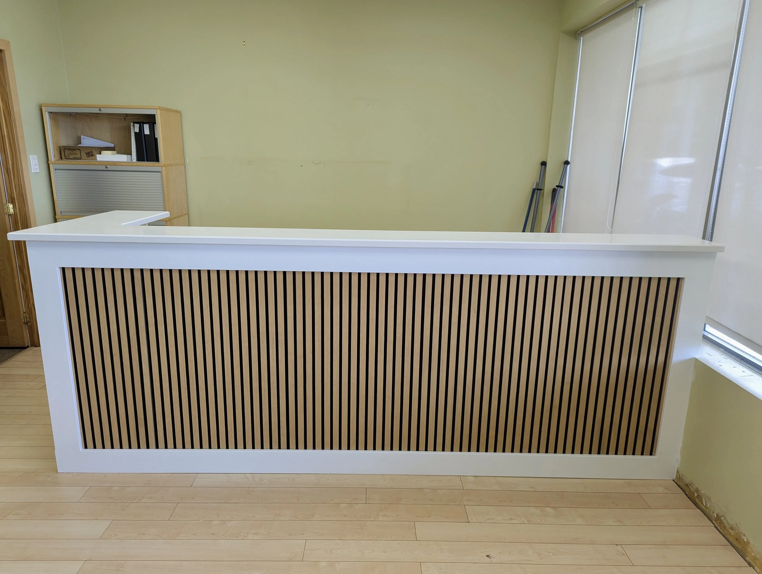 Empty reception desk with wooden paneling in a room with green walls and a window.