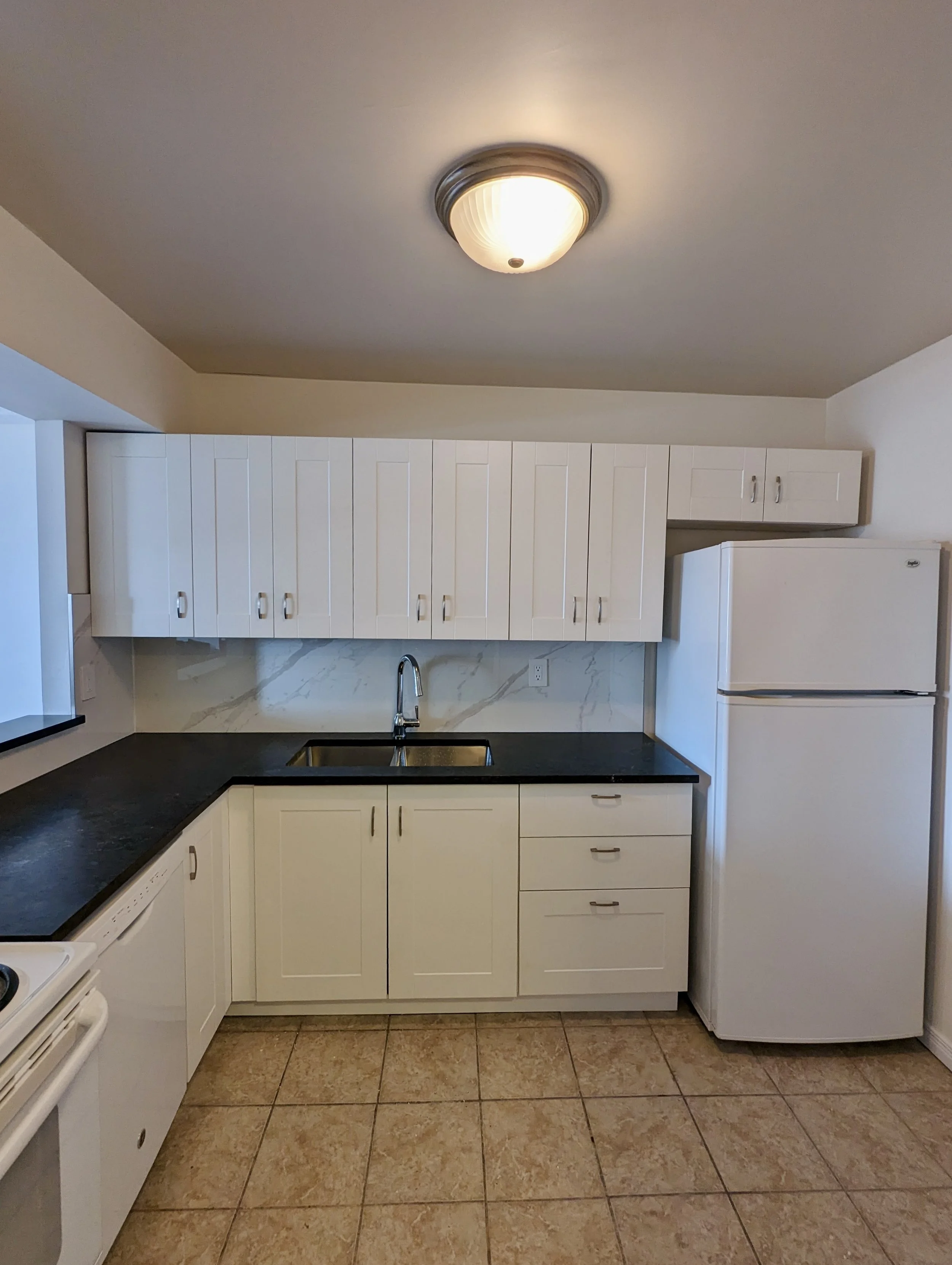 Kitchen with white cabinets, black countertop, white refrigerator, and beige tile floor.