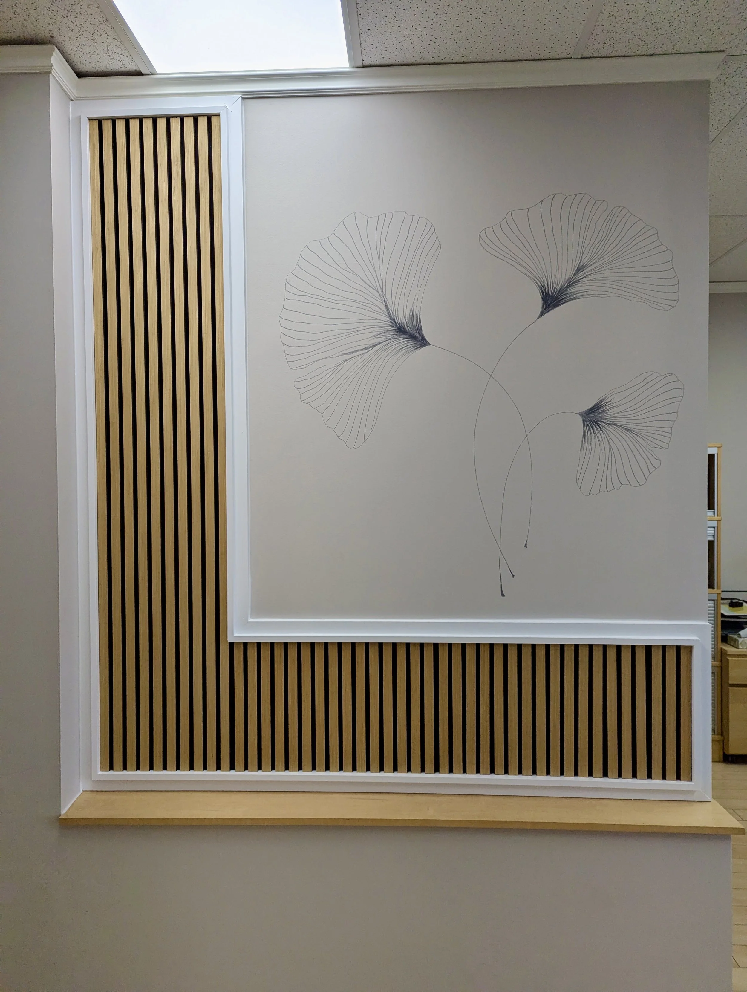 Wall with a mural of three ginkgo leaves and wood slat paneling.