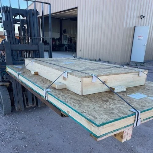 Stacked plywood sheets on a forklift, secured with straps, outside warehouse.