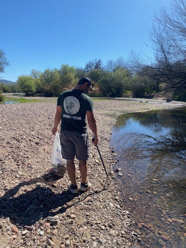 Man using a metal detector on a rocky riverbank during daytime