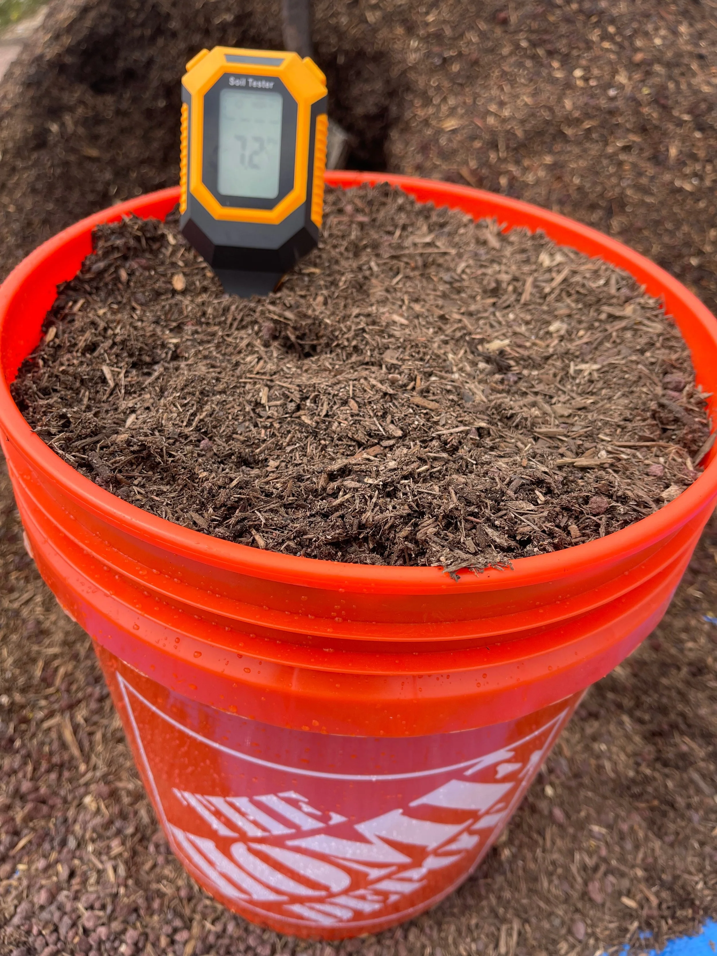 A soil tester placed on top of a bucket filled with soil, outdoors.