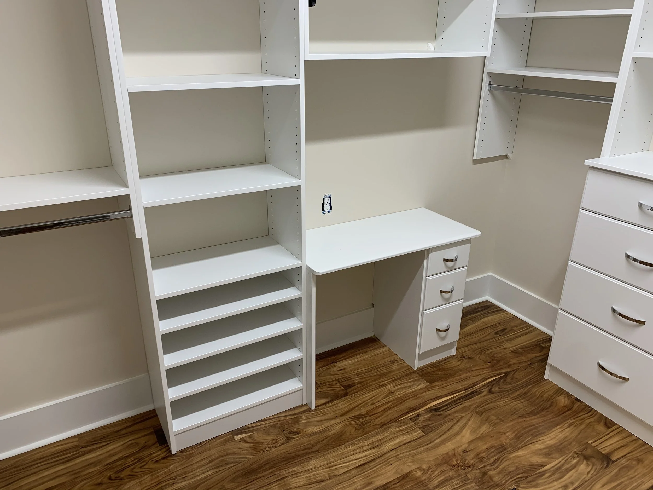 White closet shelves, drawers, and a small desk with wooden flooring.