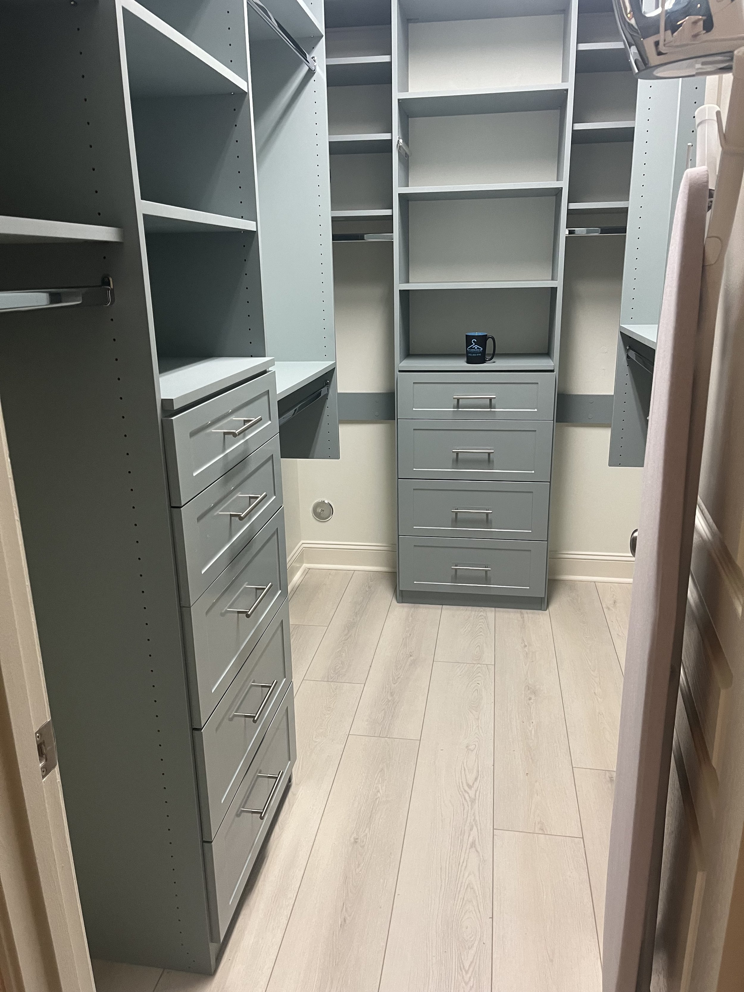 An empty walk-in closet in a new. construction home with gray shelving, drawers, and light-colored wood flooring.
