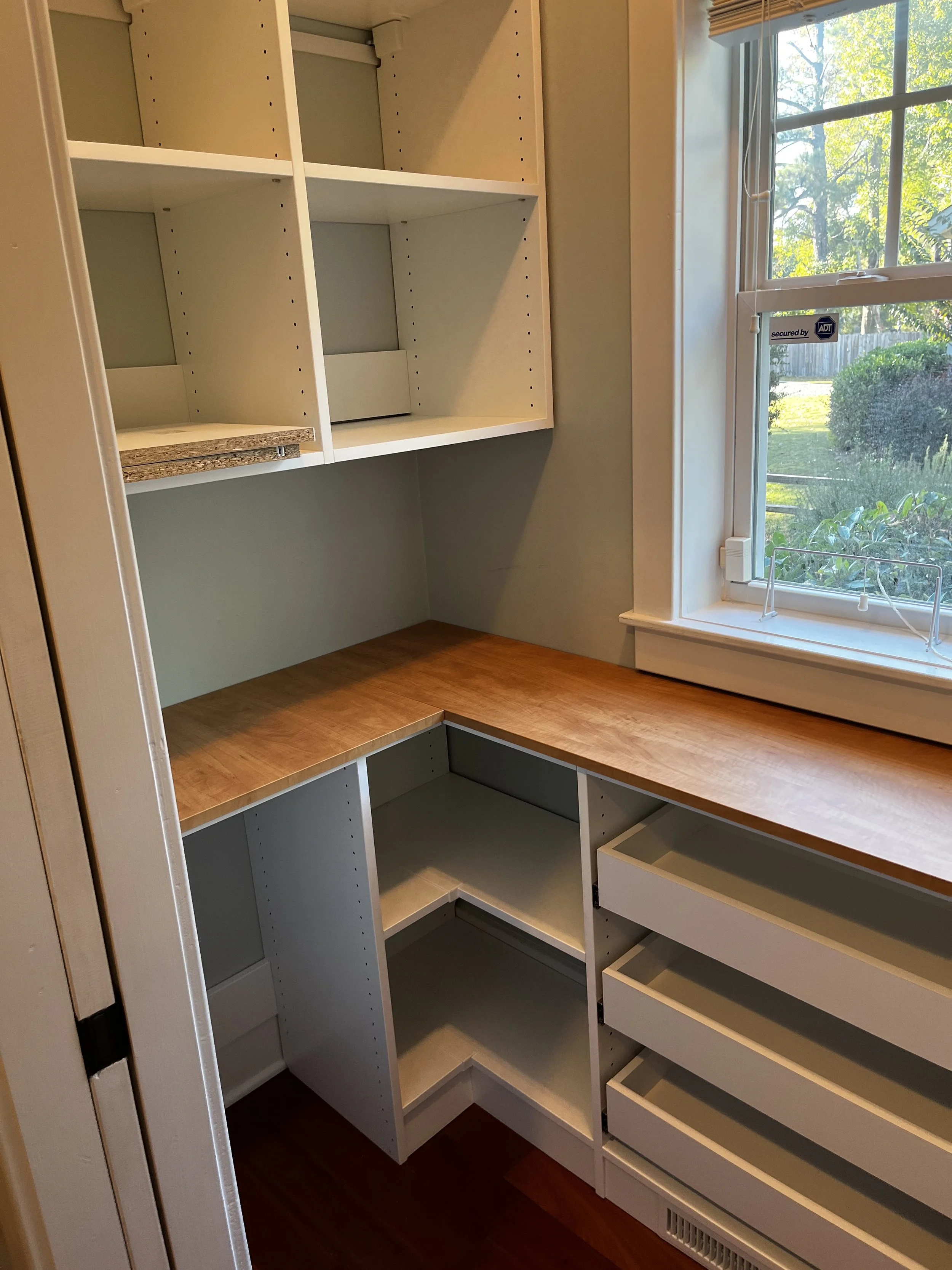Built-in corner storage and drawers with a wooden countertop near a window with sunlight.