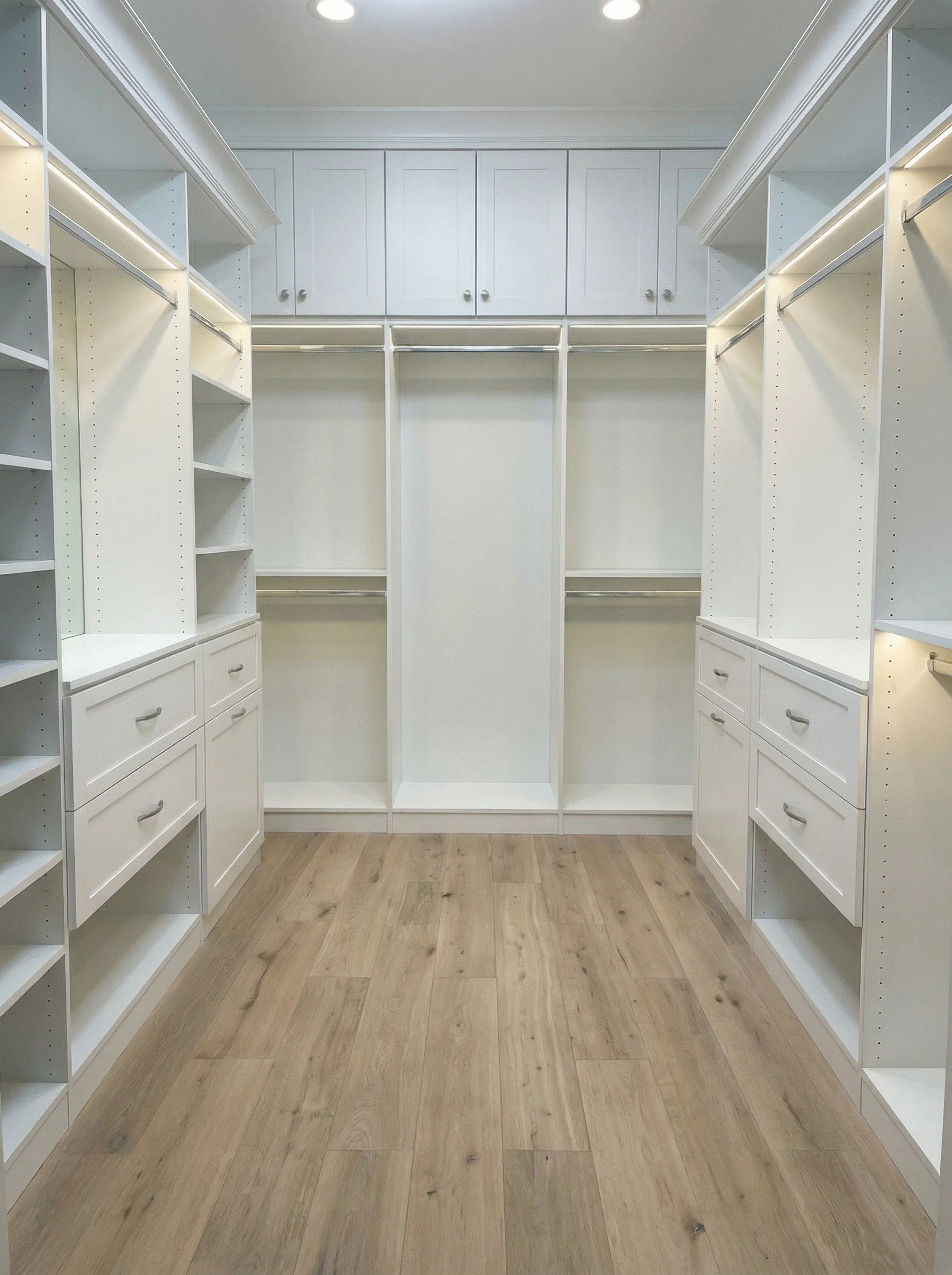 Empty custom walk-in closet with shelves, drawers, and hanging rods, finished with light wood flooring.