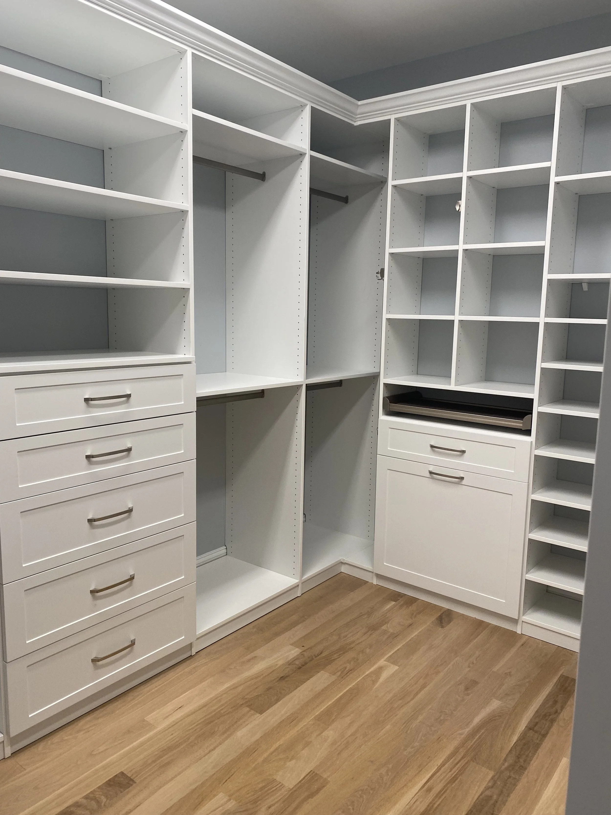 White walk-in closet design with shelves, drawers, and hanging rods, and a wooden floor.