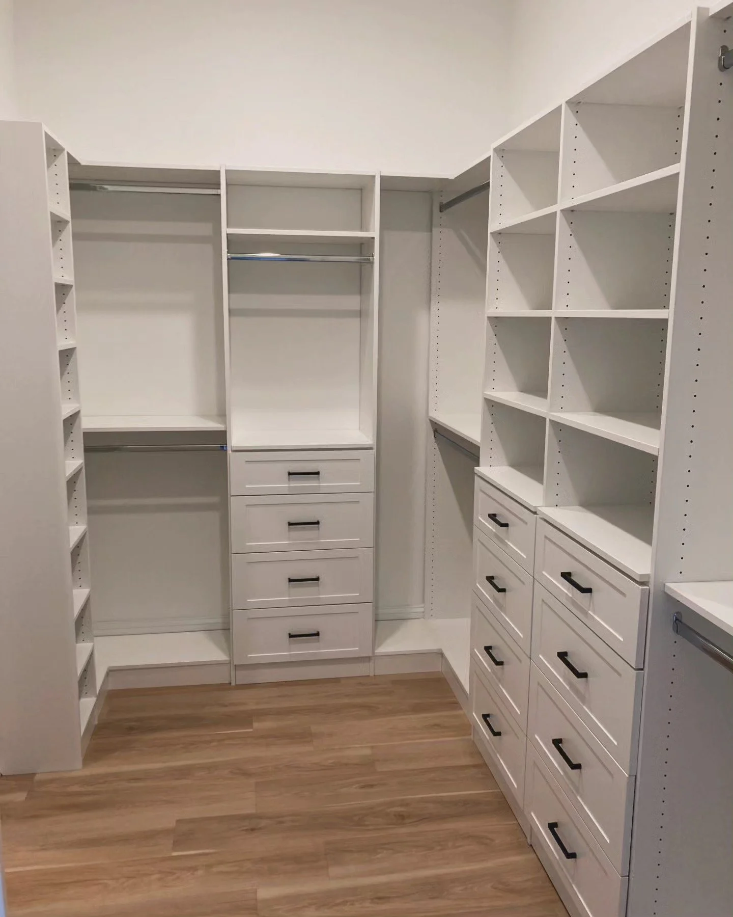 White custom walk-in closet with built-in shelves, drawers, and hanging rods, and wood flooring.