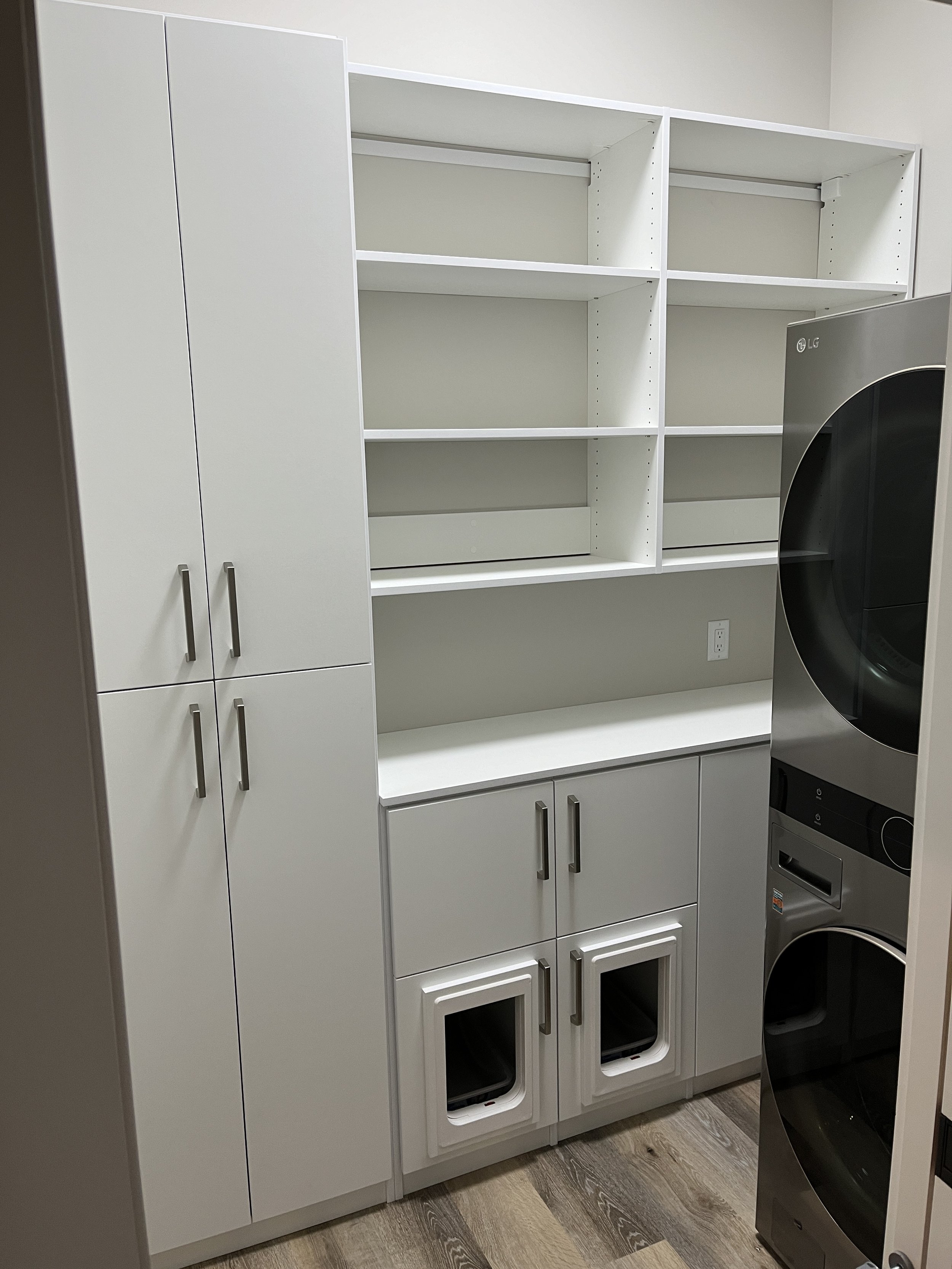 Laundry room storage design with cabinets, open shelving, and a stacked washer and dryer.