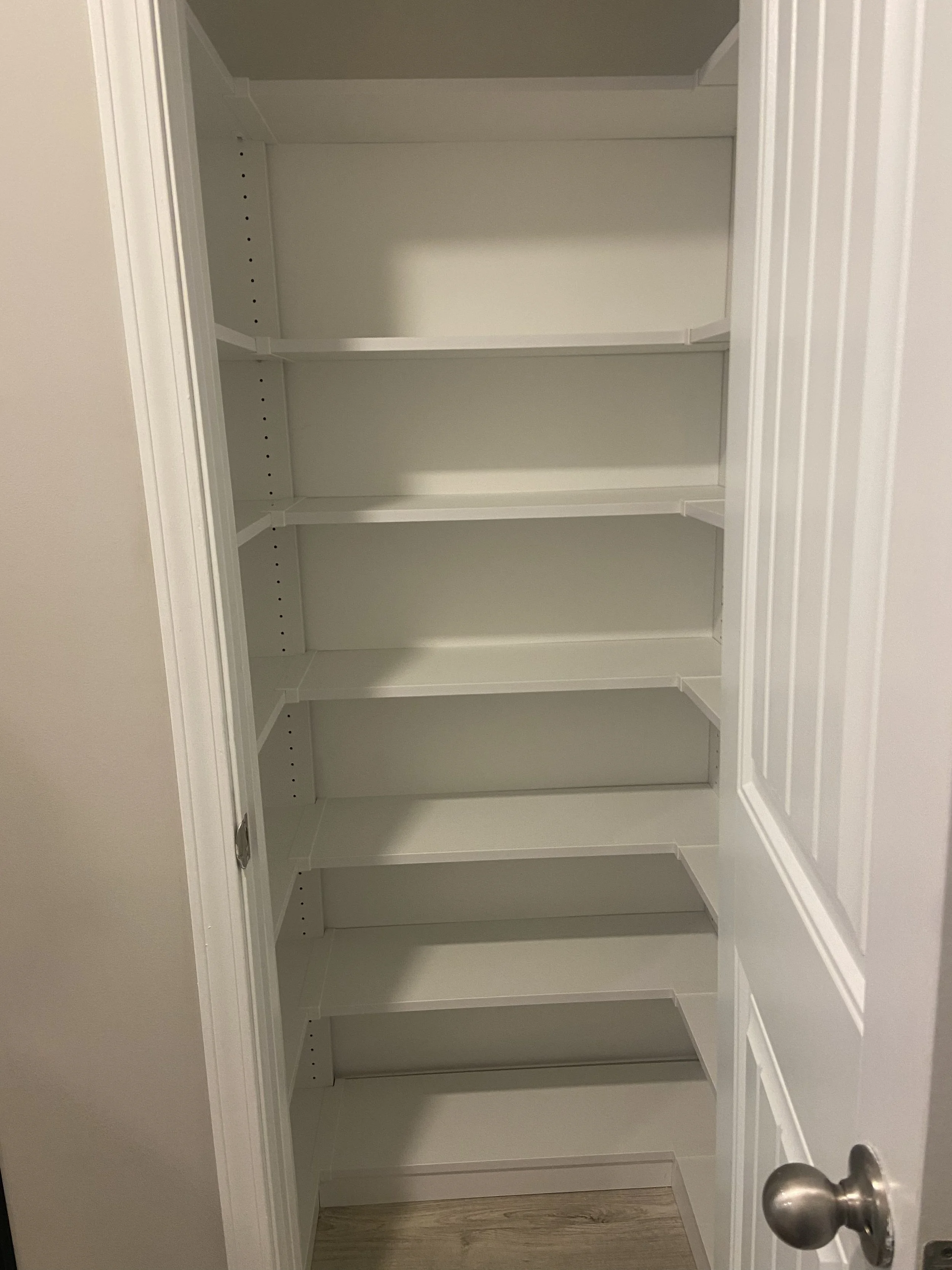 A built-in small custom pantry with shelves and a white door with a silver doorknob.