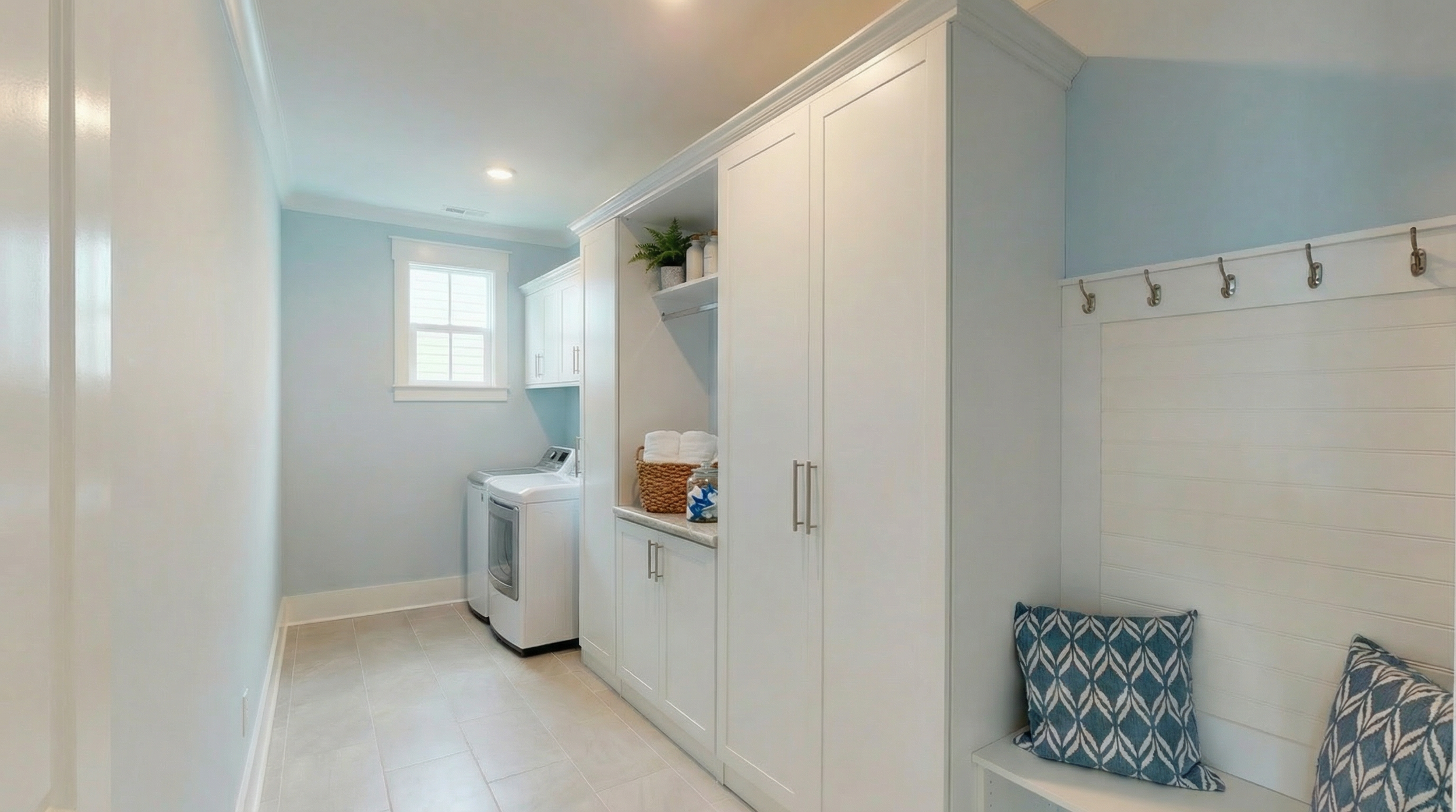 Laundry room with white cabinets, a washer and dryer, a small window, and a built-in seating area with patterned cushions.