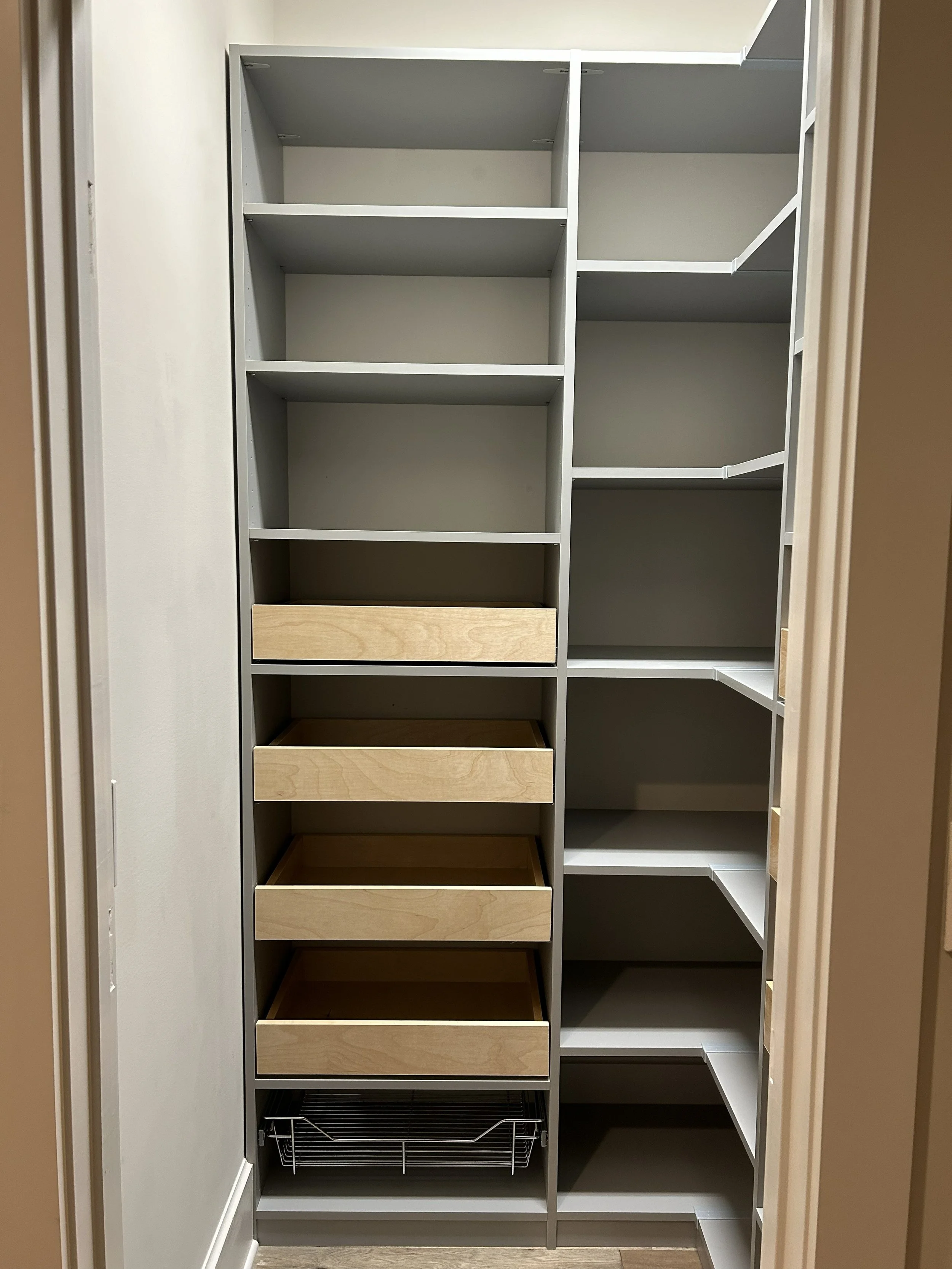 Kitchen storage closet with multiple shelving units, drawers, and wire basket at the bottom.
