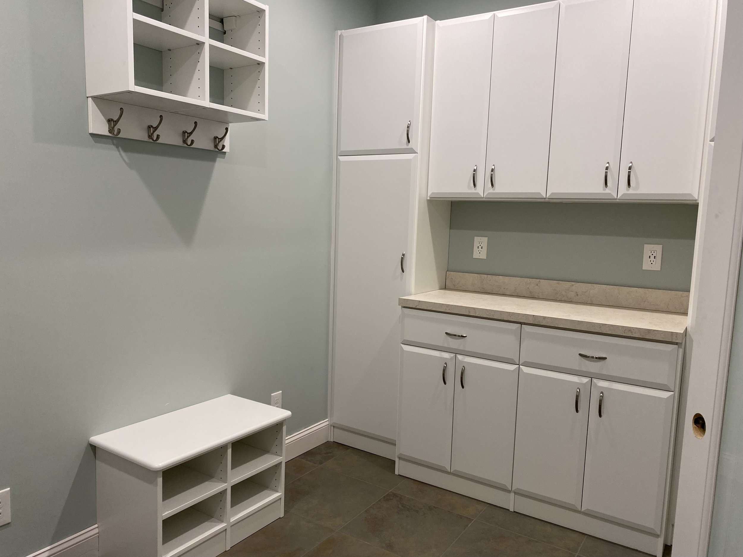 Custom storage with light green walls and white cabinets. There are upper and lower cabinets with silver handles and a beige countertop.