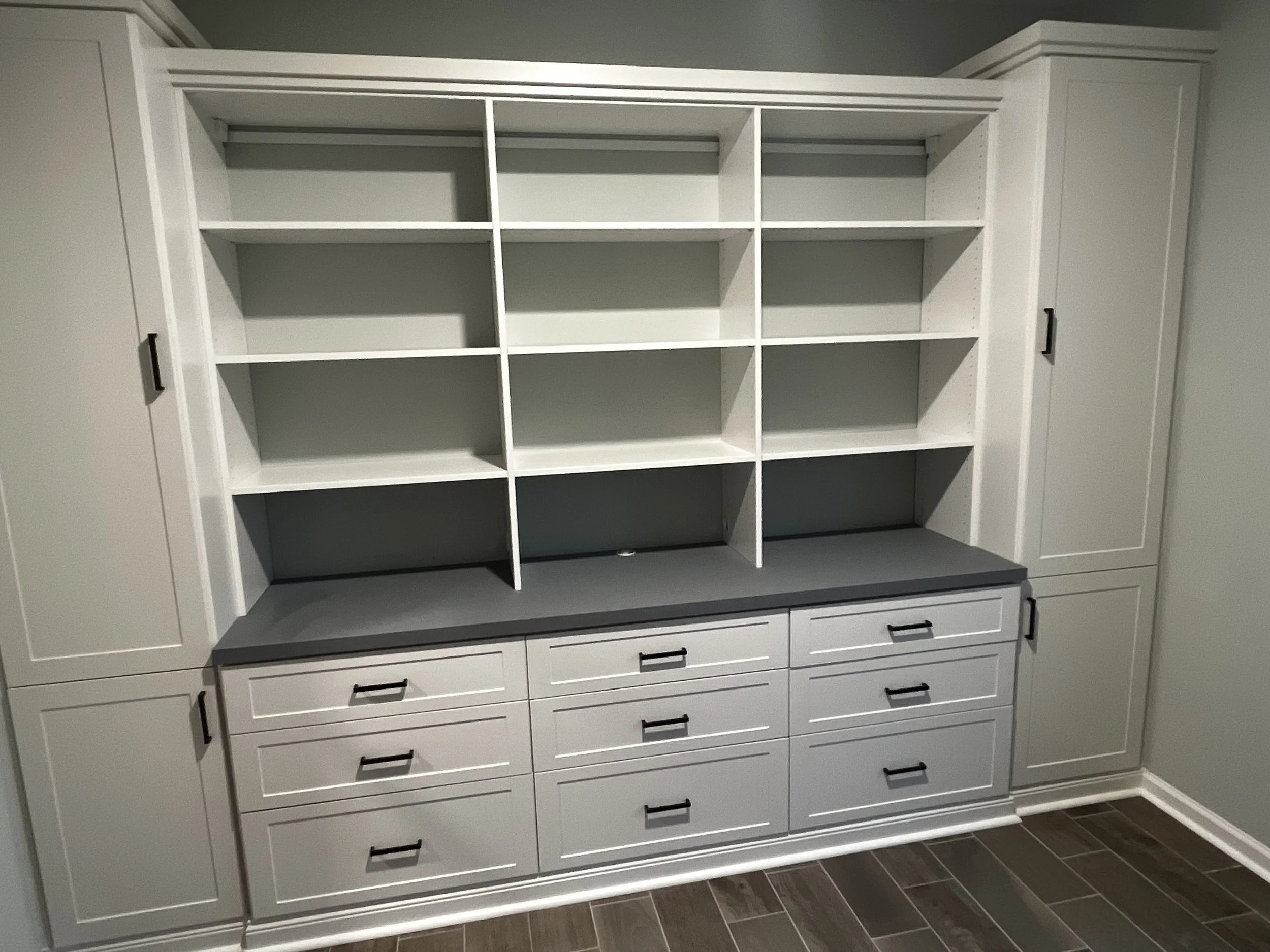 White built-in living room storage with open shelves and closed storage compartments, featuring black handles, situated on a wall with a wood floor underneath.