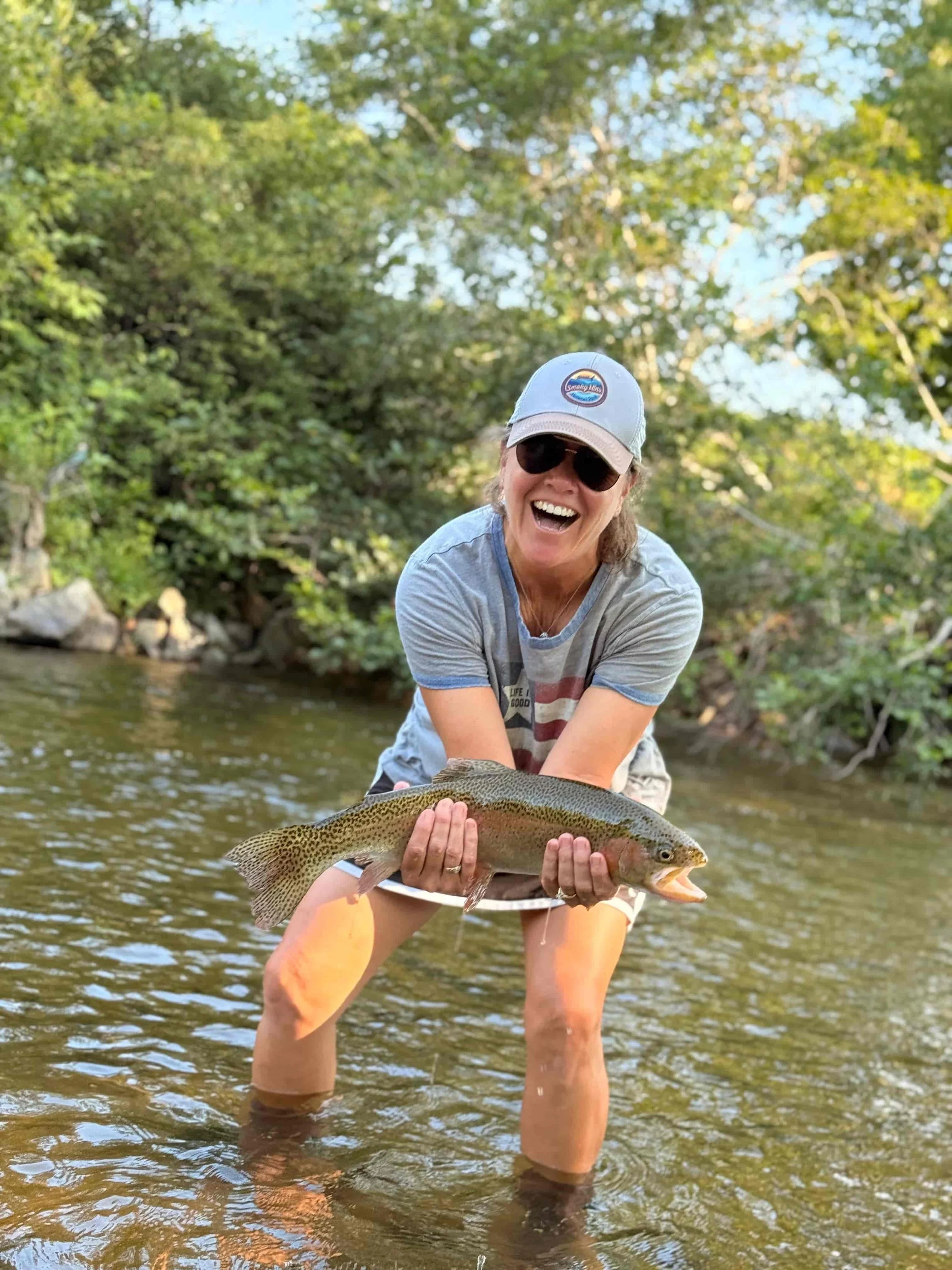 Cathy Morrison standing in a river holding a trout