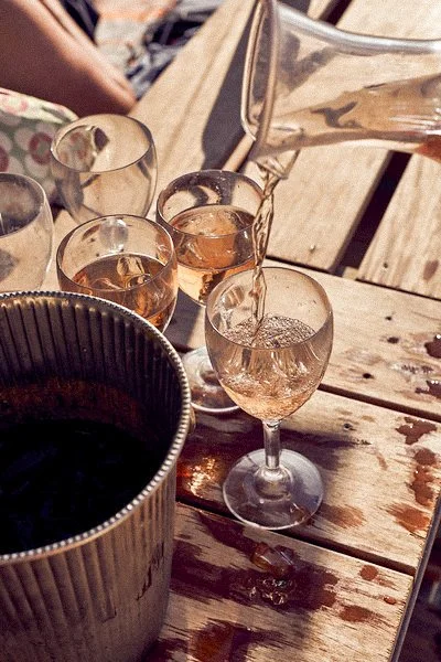 Pouring rosé wine into a glass on a wooden table with multiple glasses and an ice bucket nearby.