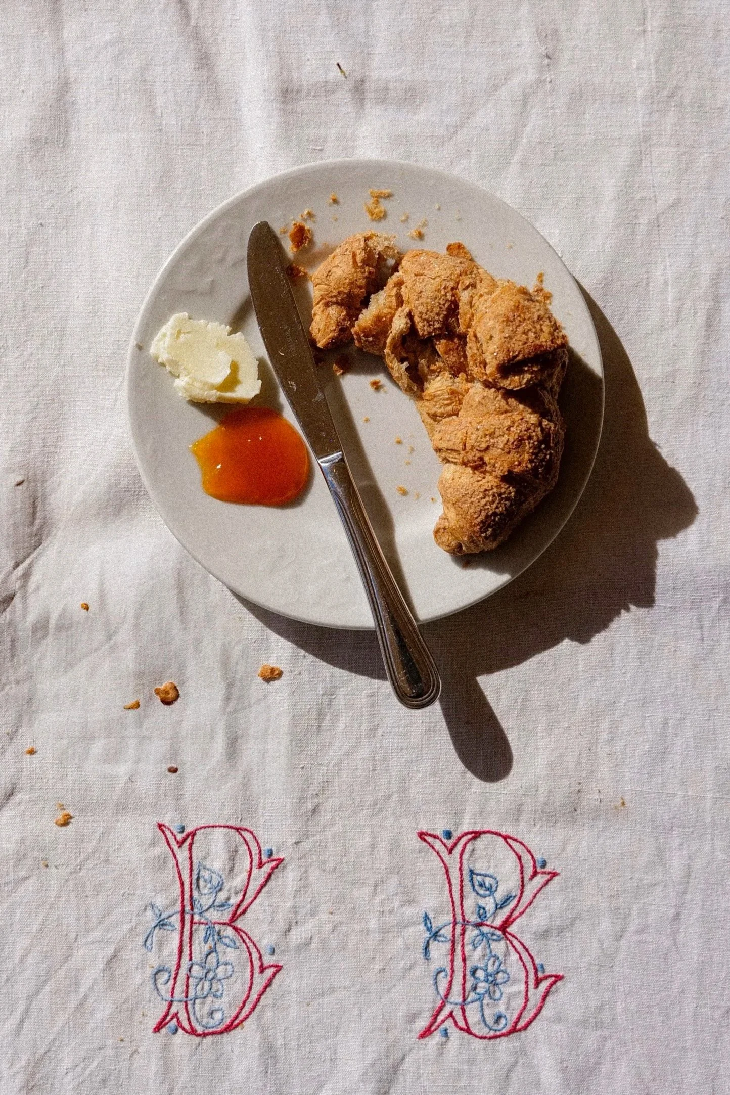 A white plate with a piece of fried chicken, a dollop of butter, and a small dollop of hot sauce on a white tablecloth with embroidered red and blue designs.
