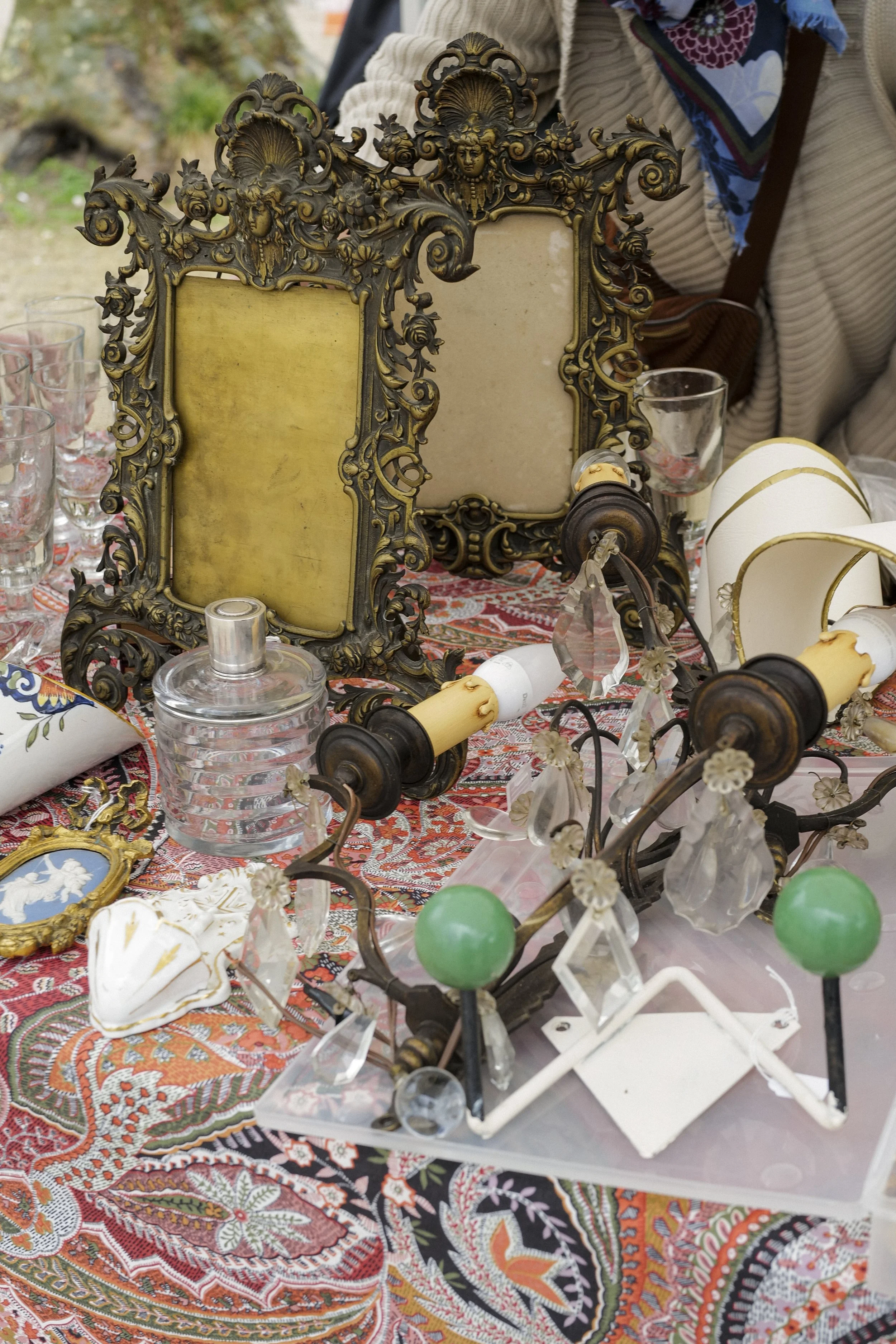Decorative vintage picture frames, glassware, and various collectibles displayed on a patterned tablecloth at an outdoor market or thrift shop.