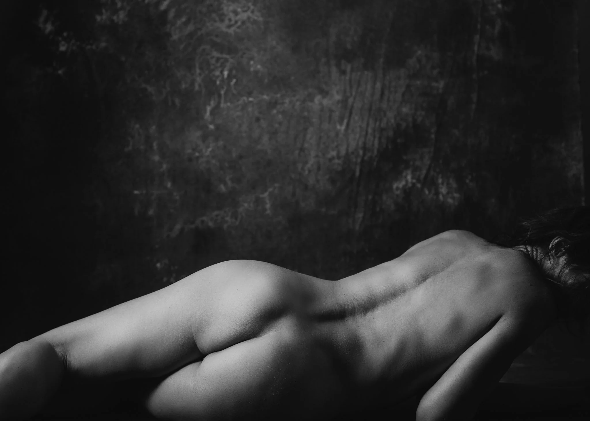 Black and white photo of a person’s torso and face, partially visible, lying on a textured surface with their arms extended outward.