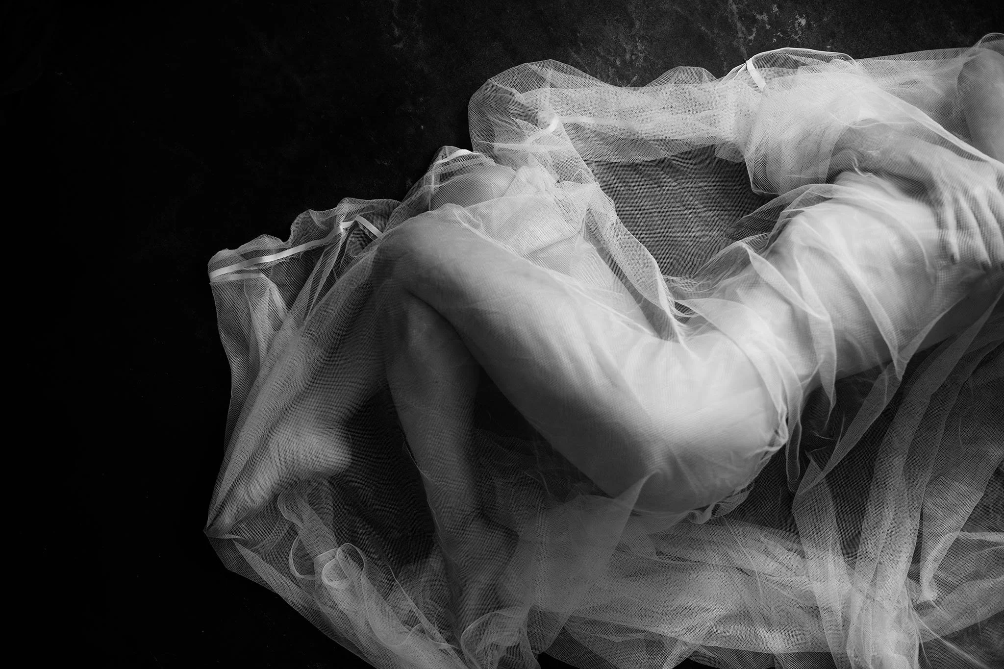 Black and white photo of a piece of delicate, sheer fabric, possibly tulle or organza, laid out on a dark surface.