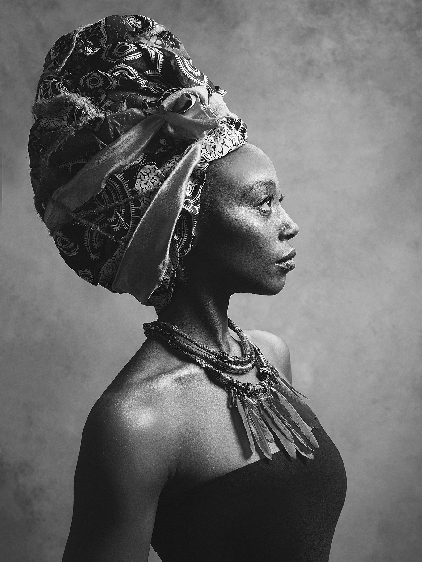 Black and white portrait of an African woman in profile wearing traditional jewelry and a patterned headwrap.